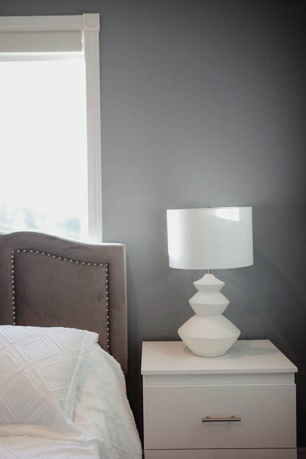 A bedroom with a bed, a bedside table with a lamp, and a window.