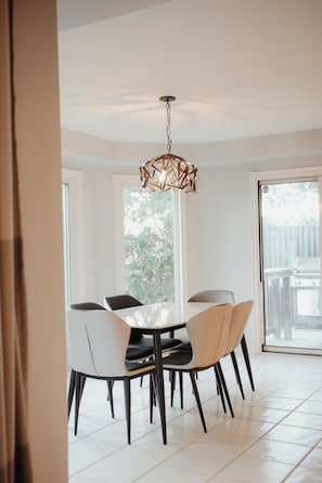 A dining area with a modern chandelier, white chairs, and a large window.