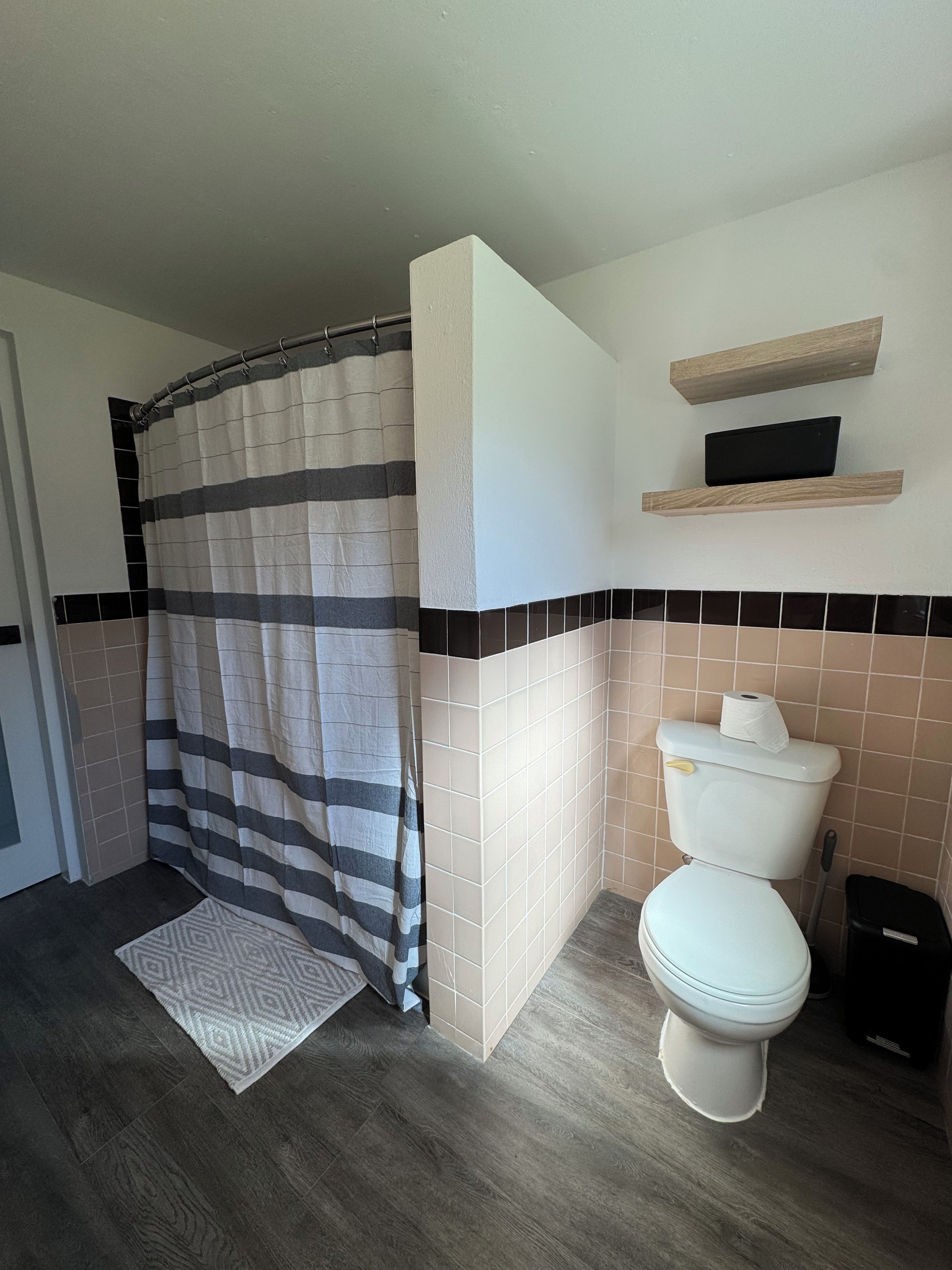 Un baño con cortina de ducha, inodoro y un estante sobre el inodoro.