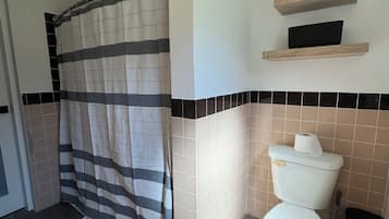 Un baño con cortina de ducha, inodoro y un estante sobre el inodoro.