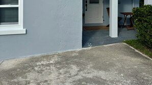 Et hus med hvide facader, en fordør og en lille veranda med et bord og stole.