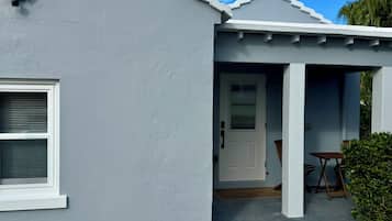 Una casa con fachada blanca, puerta principal y un pequeño porche con mesa y sillas.