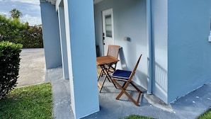 En lille, etetages bygning med en overdækket terrasse, en dør og et vindue.