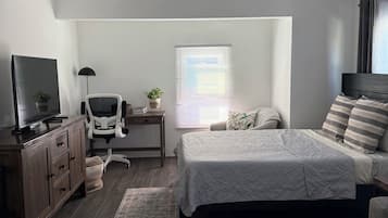 Un dormitorio con cama, escritorio, silla, televisor y ventilador de techo.