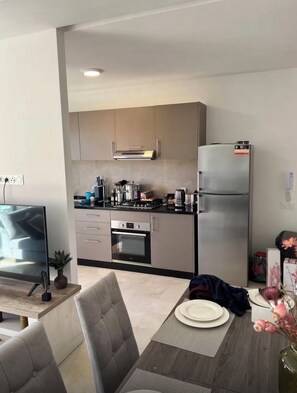 A modern kitchen with a refrigerator, oven, and gas stove. There is a dining table with chairs and a TV. - Cozy 2-bedroom apartment in marvelous Marrakech with AC (Marrakech)
