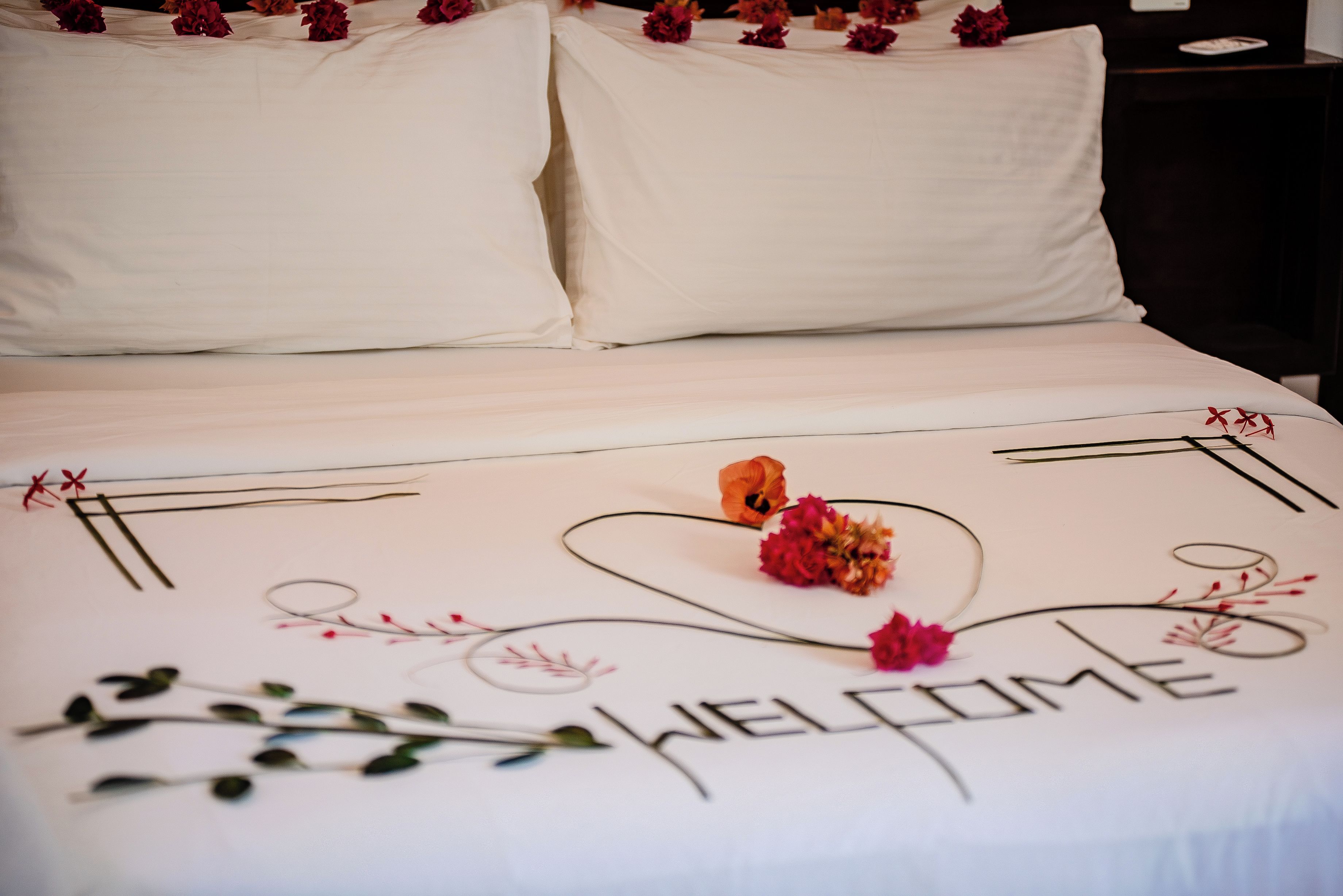 Een keurig opgemaakt bed met een 'WELCOME'-bord en decoratieve bloemen.