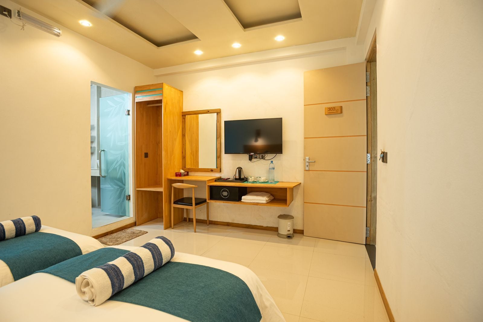 A hotel room with two beds, a desk, a television, and a bathroom door.