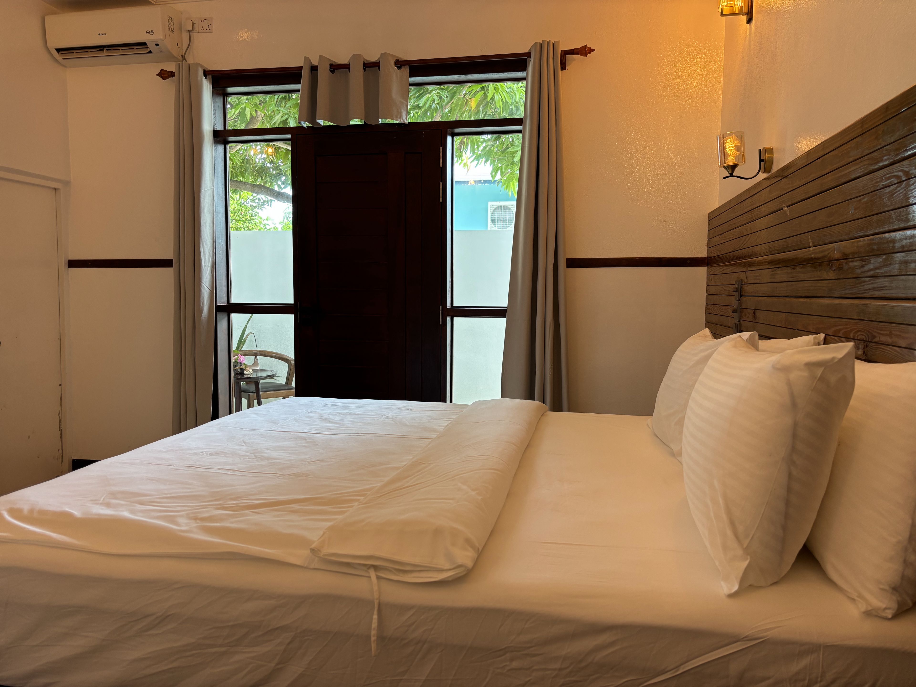 Une chambre d’hôtel avec un lit, une fenêtre avec des rideaux, un appareil de climatisation et un luminaire fixé au mur.