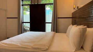 Une chambre d’hôtel avec un lit, une fenêtre avec des rideaux, un appareil de climatisation et un luminaire fixé au mur.