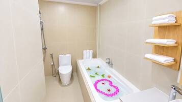 A modern bathroom with a bathtub, toilet, and shower. There are wooden shelves with towels.