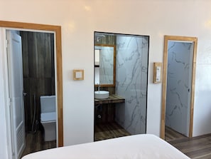 Una habitación de hotel con una cama, un baño con inodoro, lavabo y espejo.