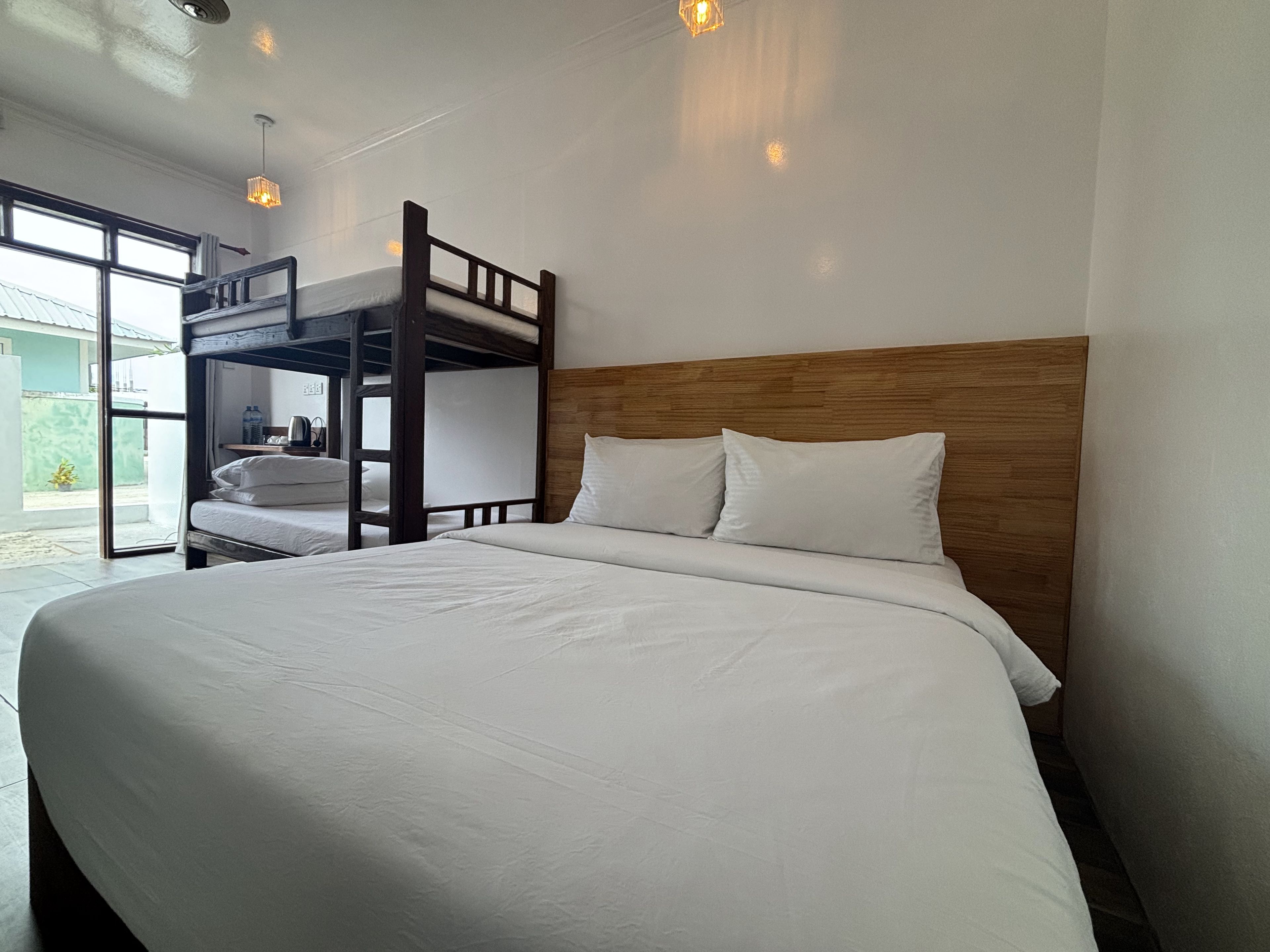 A bunk bed room with a wooden headboard, white bedding, and a view of the outside.