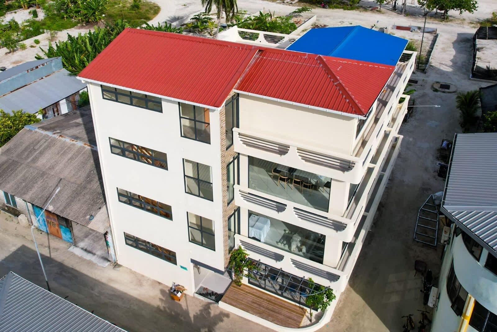 A multi-story building with a red roof, large windows, and a balcony with plants.