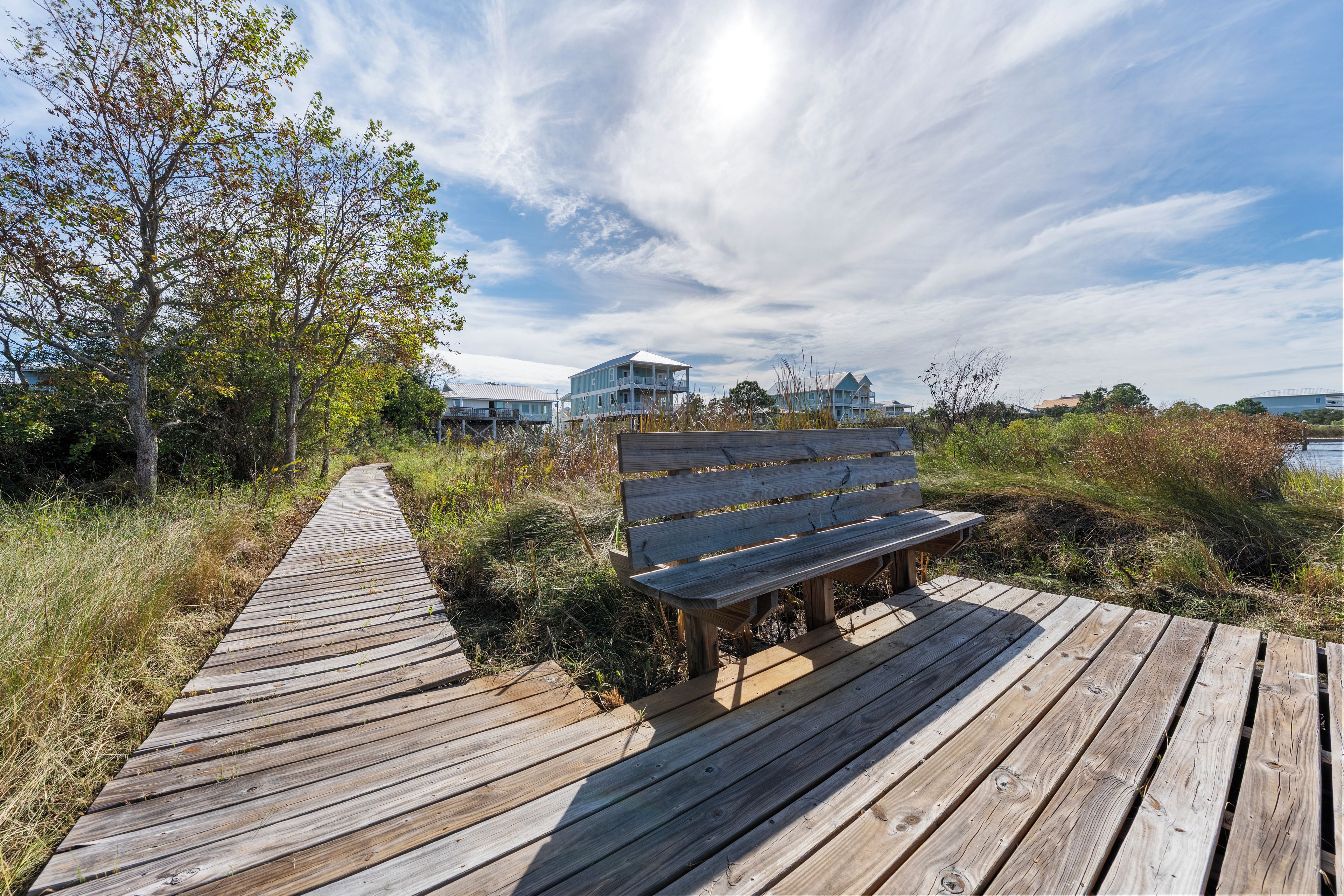 A wooden boardwalk leading to a bench with a view of a coastal building.