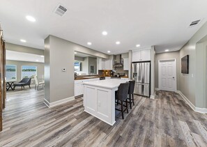 A modern kitchen with a central island, bar stools, and a stainless steel refrigerator. - Bay-view 5BR Gulf Shores Home, Sleeps 12, and Easy Beach Access (Gulf Shores)