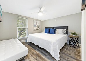 A bedroom with a bed, a ceiling fan, a window with blinds, and a small table with a plant. - Bay-view 5BR Gulf Shores Home, Sleeps 12, and Easy Beach Access (Gulf Shores)