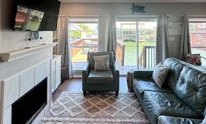 A living room with a fireplace, a sofa, a chair, and a television. - Spacious 3-bedroom waterfront condo on the island. (Corpus Christi)