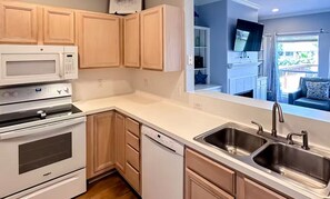 A modern kitchen with white appliances, wooden cabinets, and a large window. - Spacious 3-bedroom waterfront condo on the island. (Corpus Christi)
