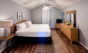 A bedroom with a bed, bedside table, lamp, dresser, mirror, ceiling fan, and a window with blinds. - Spacious 3-bedroom waterfront condo on the island. (Corpus Christi)