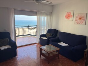 A living room with a view of the beach, a ceiling fan, and two framed flowers on the wall. - Gandia Beach, First-Line Beachfront (Grau i Platja)