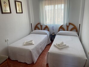A hotel room with two single beds, a small table with a lamp, and a window with sheer curtains. - Gandia Beach, First-Line Beachfront (Grau i Platja)