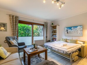 A bedroom with a bed, a sofa, a table, a bookshelf, and a window with curtains. - Holiday Apartment 3 "little Seagull" (St. Peter-Ording)