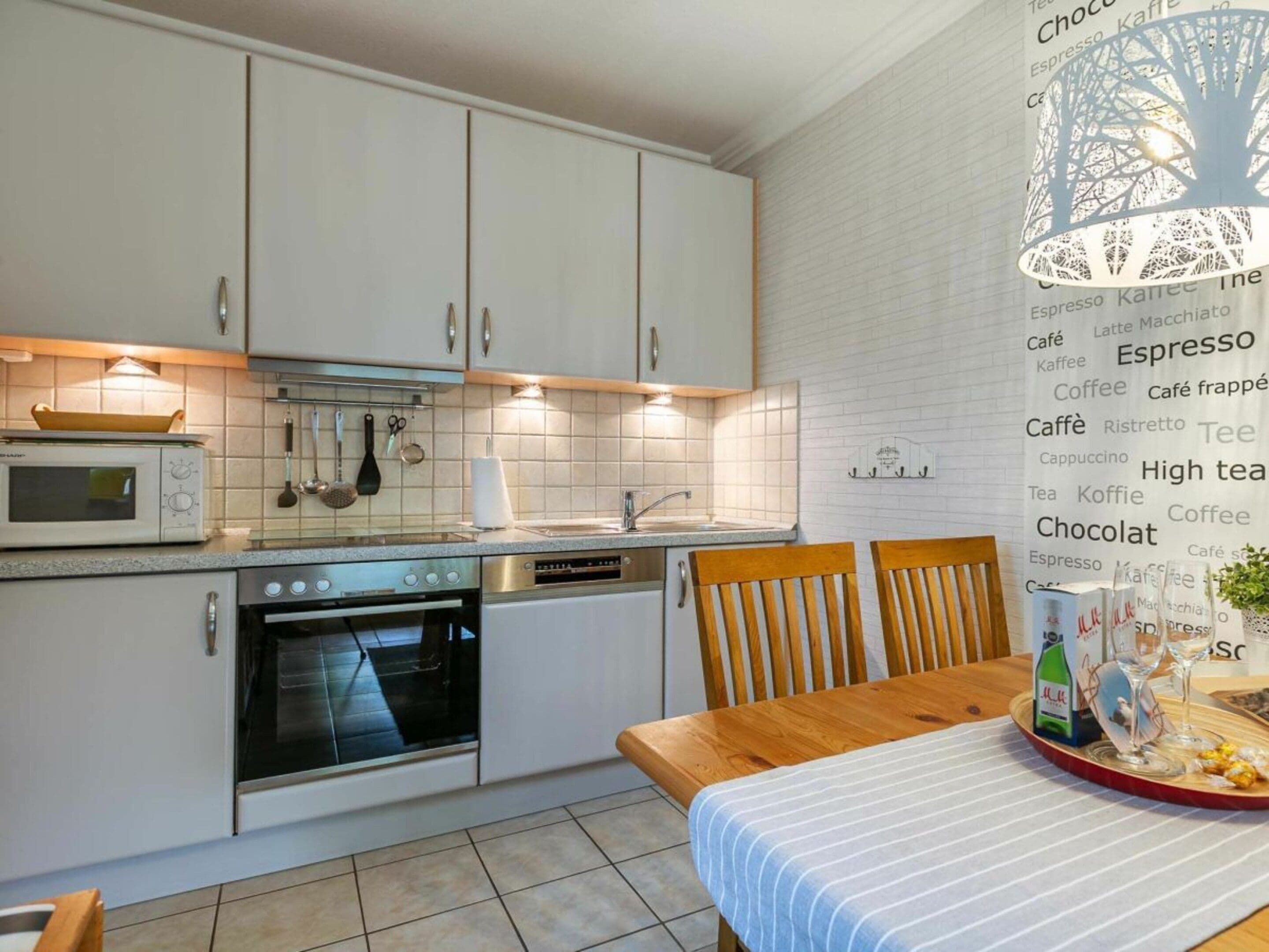 A modern kitchen with white cabinets, a microwave, an oven, and a sink. There is a dining table with chairs and a decorative item on the table.