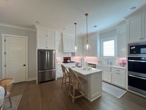 A modern kitchen with white cabinetry, stainless steel appliances, and a central island with bar stools. - Spacious 4-bedroom house on the Country Club. Less than 2mi from the stadium! (Oxford)