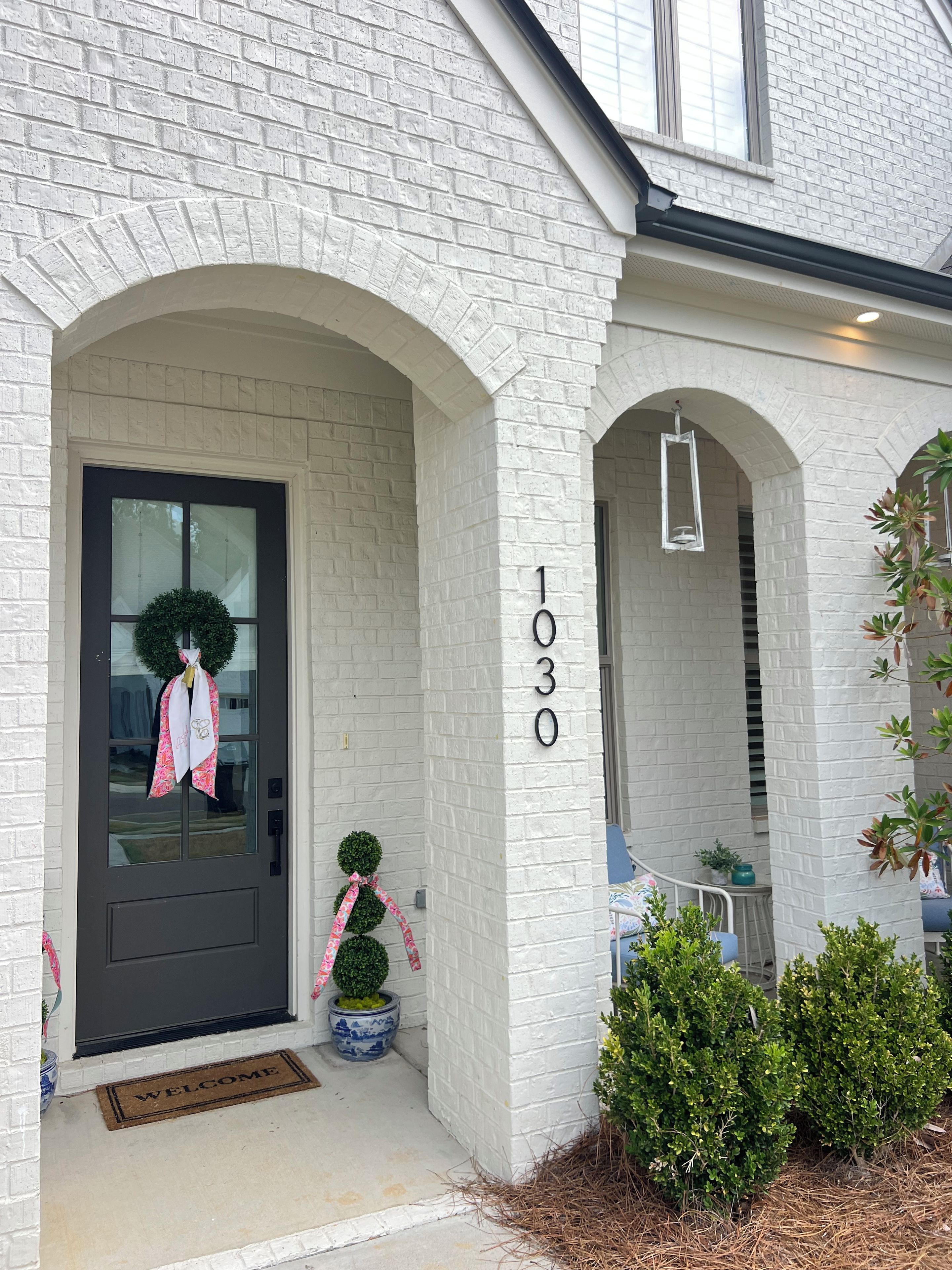 A white brick house with a dark front door, a welcome mat, and a number '1030' on the wall.