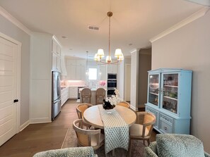 A kitchen with white cabinets, a dining table with chairs, a chandelier, and a blue cabinet with glass doors. - Spacious 4-bedroom house on the Country Club. Less than 2mi from the stadium! (Oxford)