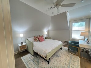 Une chambre à coucher avec un lit, des lampes de chevet, un bureau, une chaise et un ventilateur de plafond.