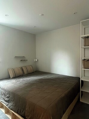 Ein Schlafzimmer mit einem Bett, einem Nachttisch, einem Wandregal und einem weißen Kleiderschrank.