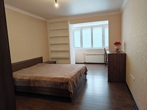 Une chambre à coucher avec un lit, un radiateur, une fenêtre et une petite table sur laquelle se trouve un vase.