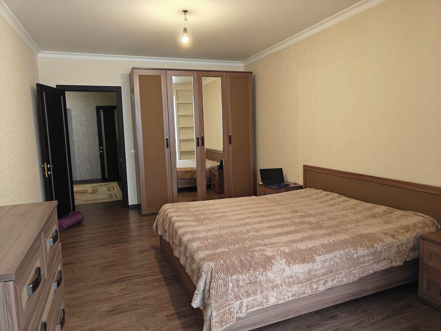 A bedroom with a bed, a desk, a wardrobe, and a door leading to a bathroom.