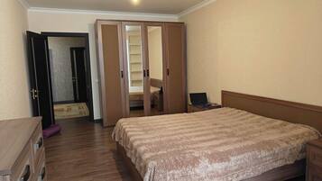 A bedroom with a bed, a desk, a wardrobe, and a door leading to a bathroom.