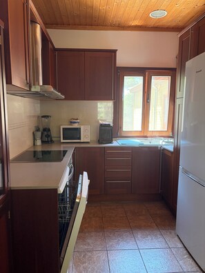 A kitchen with wooden cabinets, a microwave, a stove, and a window. - Casa Bolets - A house in the woods near the best beaches in southern Catalonia (L'Ametlla de Mar)