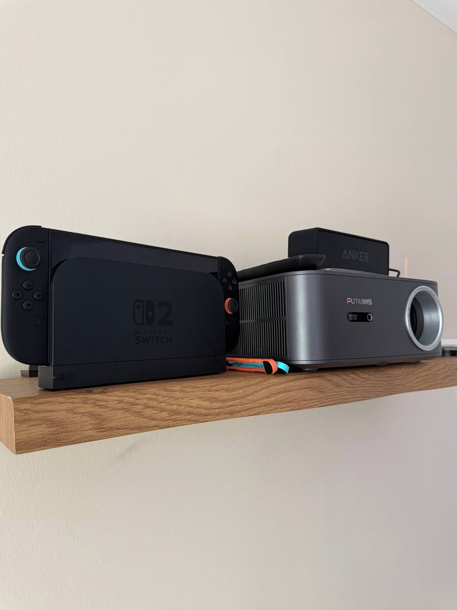 Une console Nintendo Switch et un haut-parleur Puttyms Anker sur une étagère en bois.