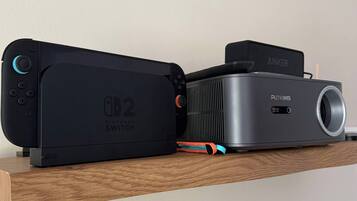 Une console Nintendo Switch et un haut-parleur Puttyms Anker sur une étagère en bois.