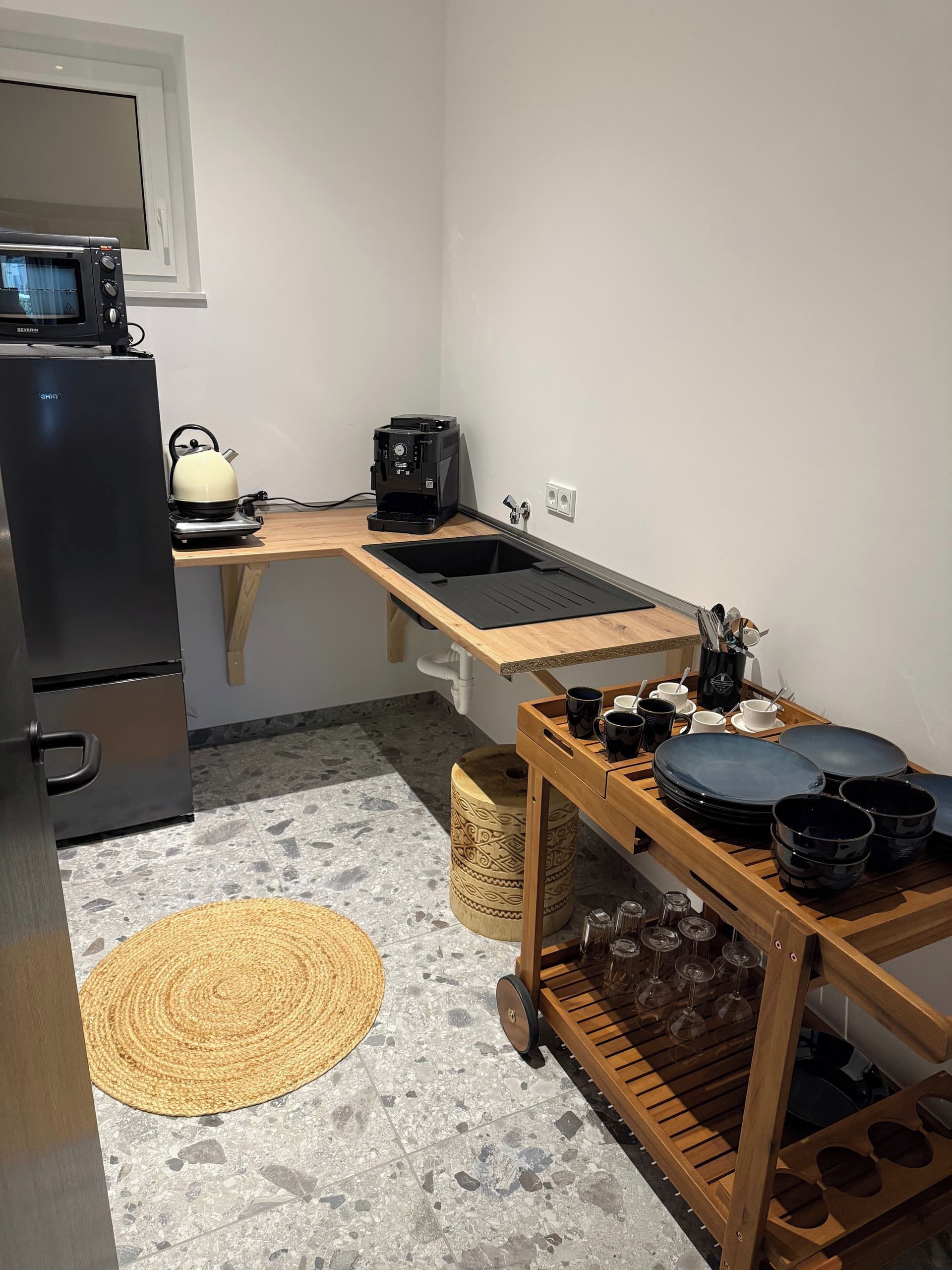 Une cuisine compacte équipée d’un réfrigérateur, d’une bouilloire, d’une machine à café et d’une table en bois avec de la vaisselle et des verres.