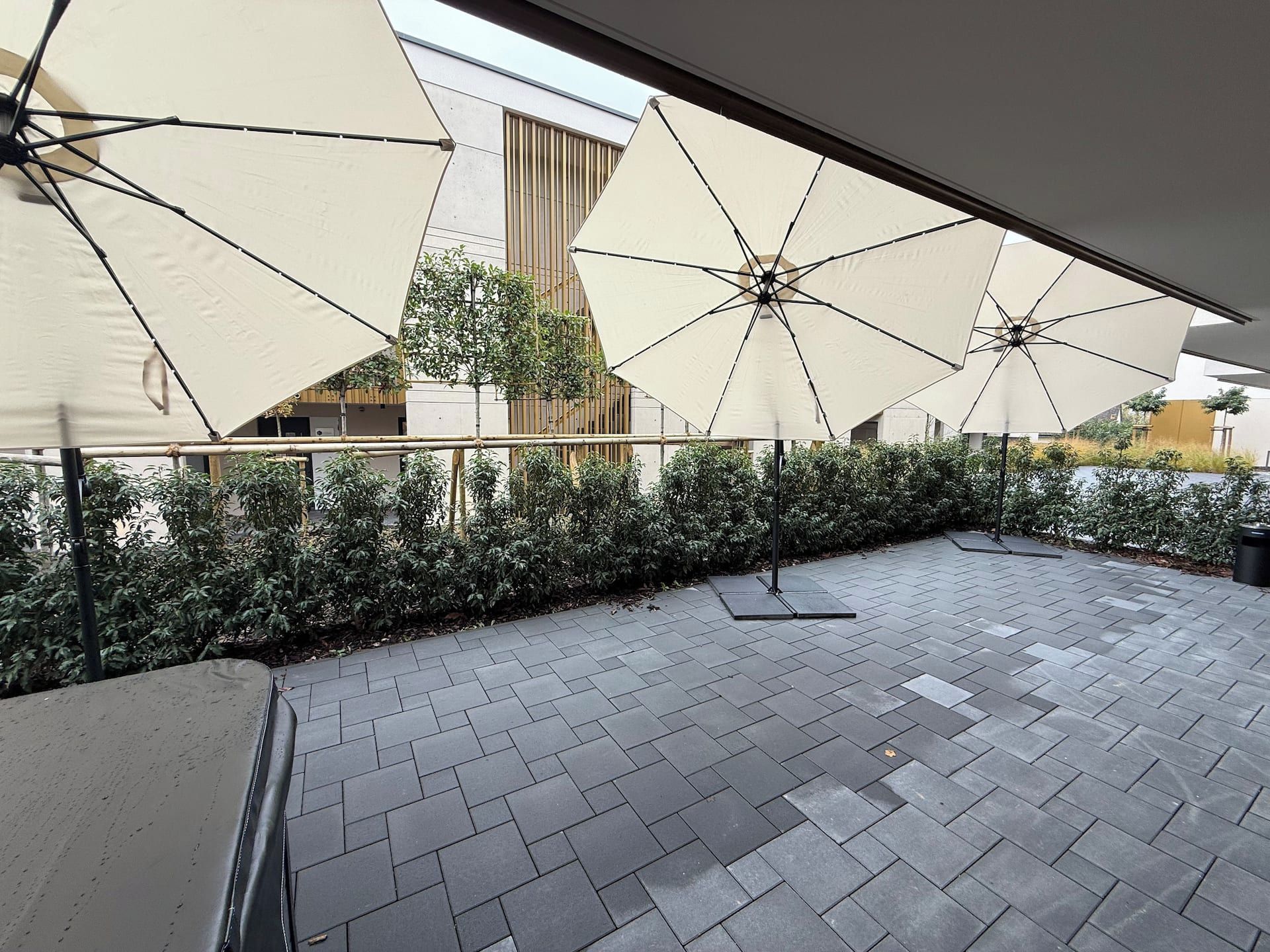 An outdoor patio area with tiled flooring and multiple large umbrellas providing shade.