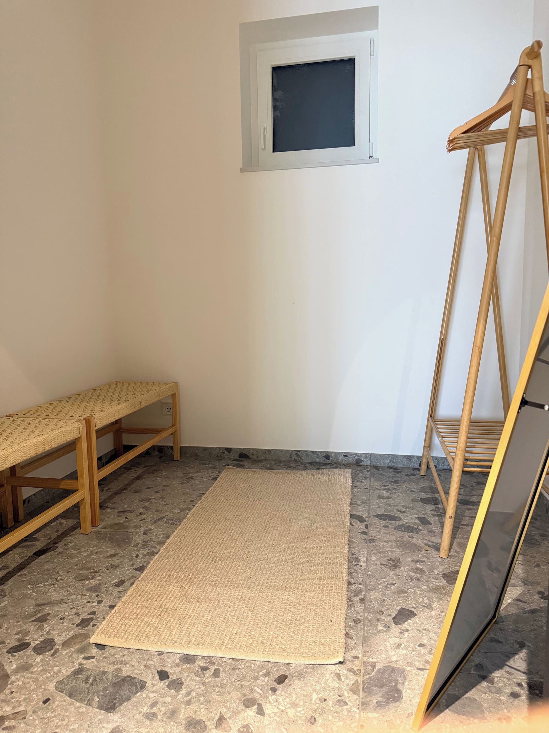 A room with a bench, a mat, a wooden stand, and a window.