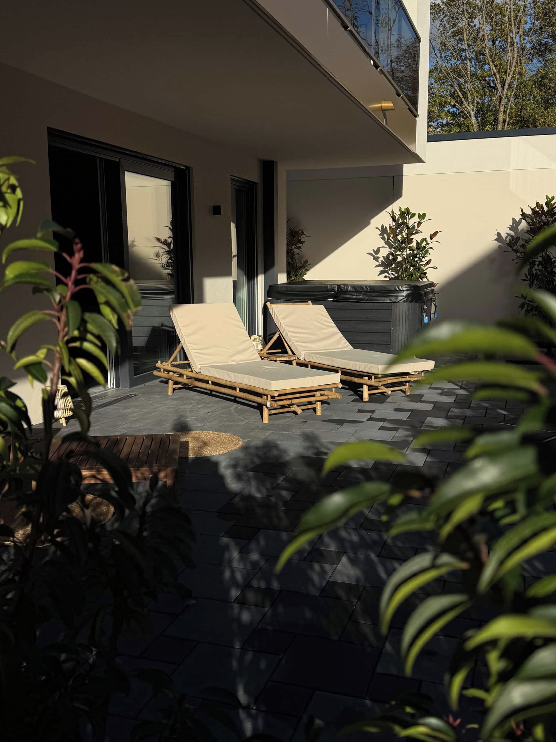 Un espace de détente extérieur moderne, avec deux fauteuils et une petite table, entouré de plantes en pot et doté d’un sol en pierre.