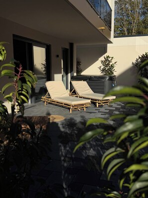 Een modern buitenzitgedeelte met twee loungestoelen en een bijzettafeltje, omringd door potplanten en een stenen vloer.