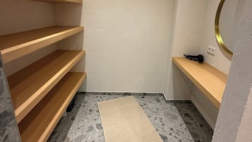 Een kleine, lege kamer met houten planken, een spiegel en een vloerkleed op een geruite vloer.