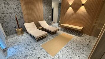 Un spa moderno con dos sillones reclinables, un banco de madera y suelo de piedra.