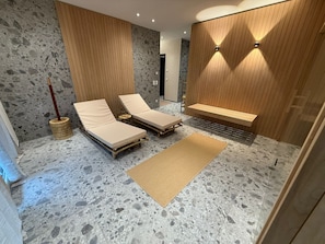 A modern spa room with two lounge chairs, a wooden bench, and a stone floor. - KaiserLogen Wellness — a private spa oasis with an XXL sauna and outdoor hot tub (Kaisersesch)