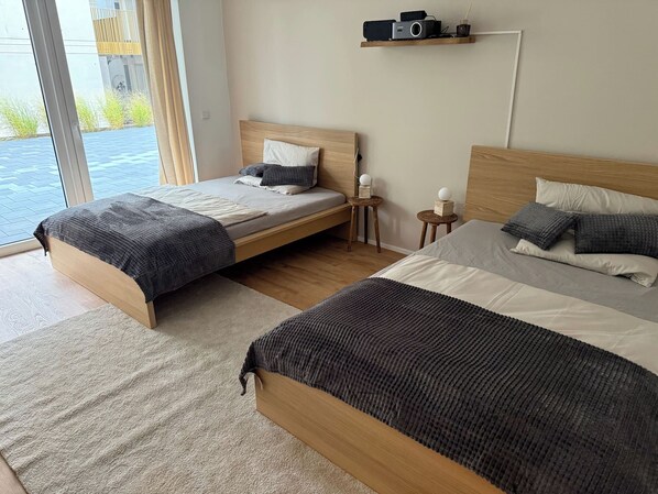 Een moderne hotelkamer met twee éénpersoonsbedden, een klein nachtkastje, een plank met elektronische apparaten en uitzicht op het groen.
