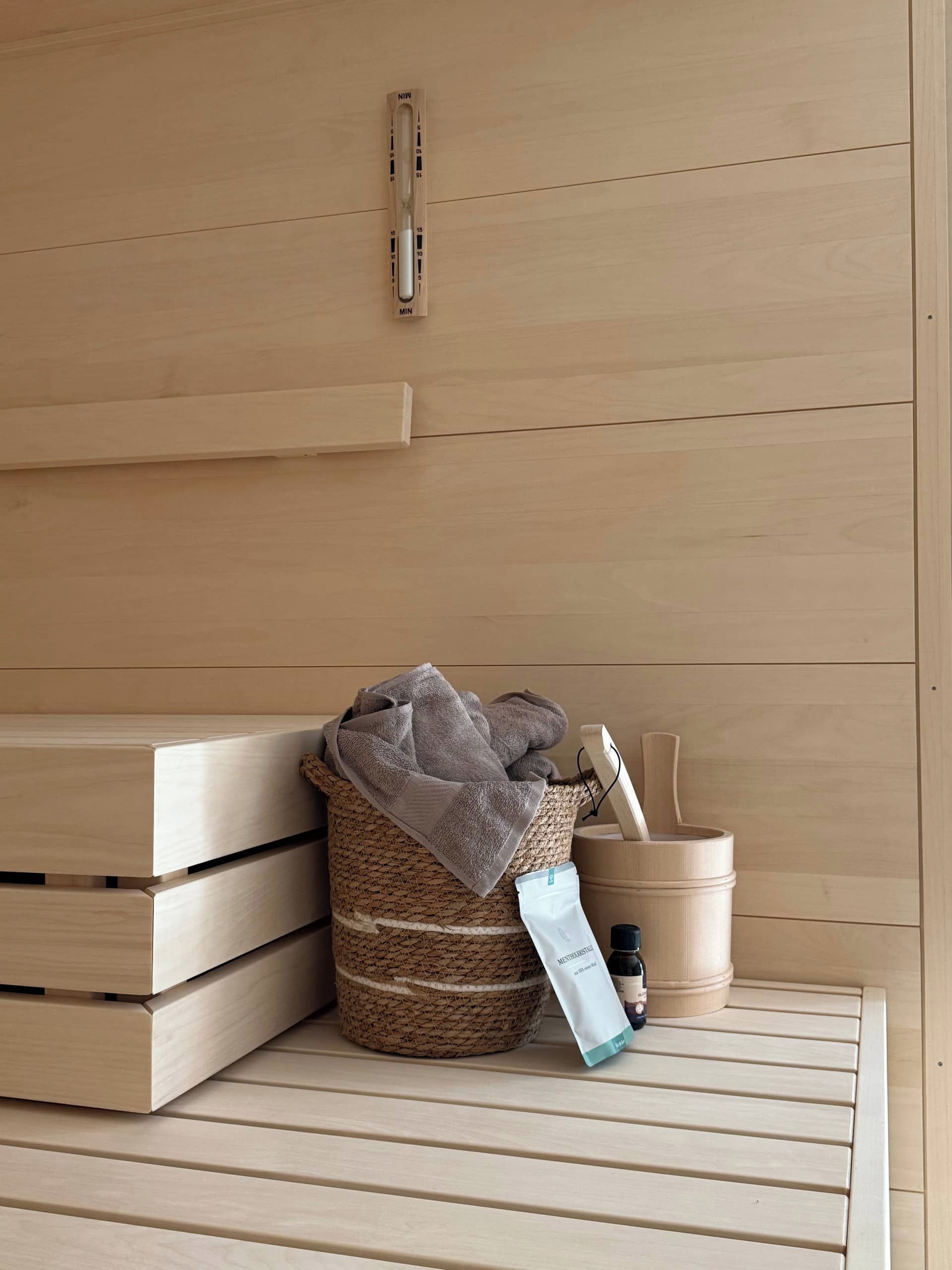 Eine Holzbank mit einem gewebten Korb, der Handtücher und eine Shampoo-Flasche enthält.