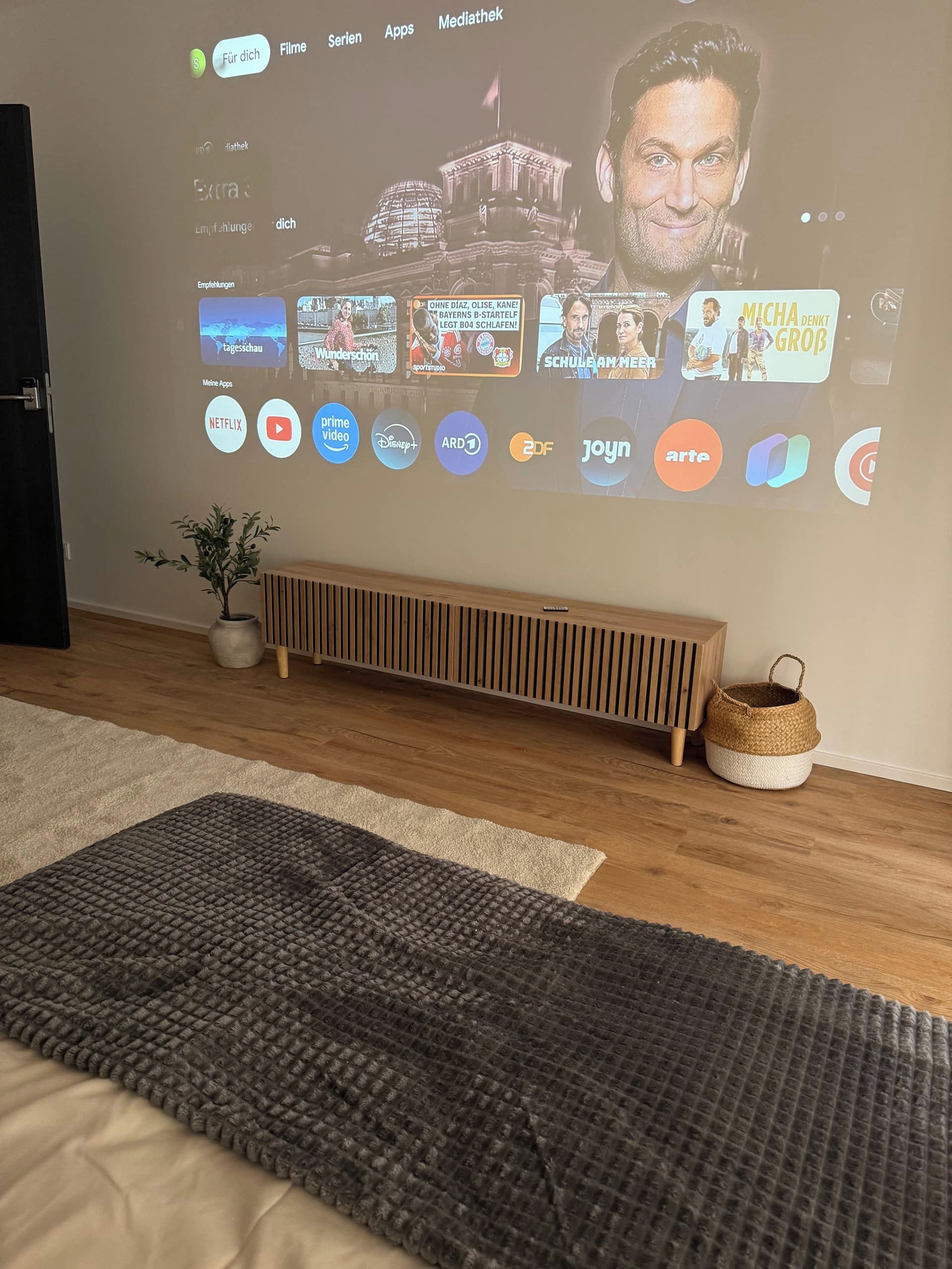 A living room with a large screen displaying various apps and a television channel interface.