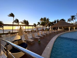 A poolside area with lounge chairs, a thatched-roof structure, and a view of the ocean. - Beachfront 2-Bedroom Condo, Ocean and Island Views, Jacuzzi – Mazatlán (Mazatlán)